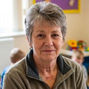 Slightly smiling older woman with short, salt-and-pepper hair, sitting in a children's playroom